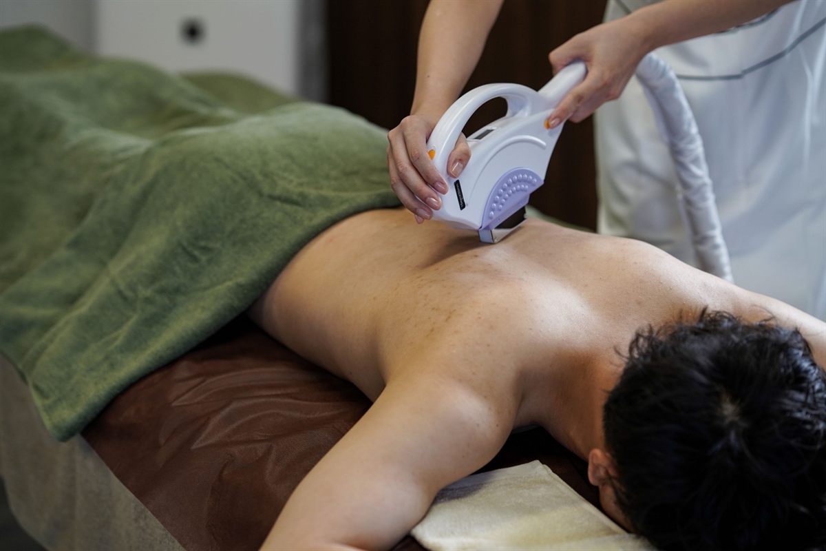 うつ伏せの男性の背中に、光脱毛の機器を当てている施術の様子